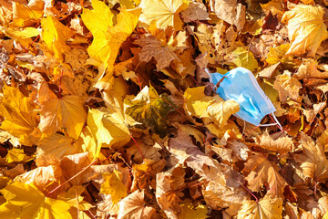 Used medical mask on autumn leaves in park