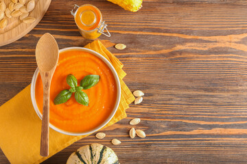 Bowl with tasty pumpkin cream soup, spices and seeds on wooden background