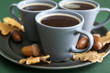 Cups of coffee with acorns and autumn leaves on green background, closeup
