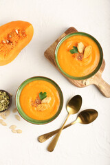 Bowls with delicious pumpkin cream soup and seeds on light background