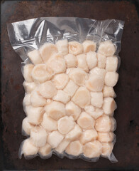 Frozen meat scallop in vacuum package. Raw delicatessen seafood.  dark background. Selective focus, top view and copy space