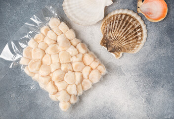 Frozen meat scallop in vacuum package and empty shells. Raw delicatessen seafood on a concrete or stone background. Selective focus, top view and copy space