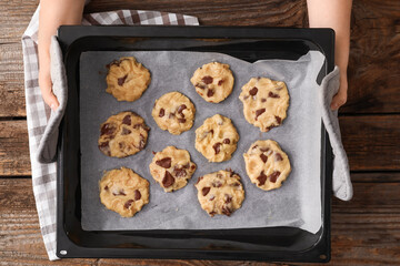 Woman with uncooked cookies in baking tray on wooden background