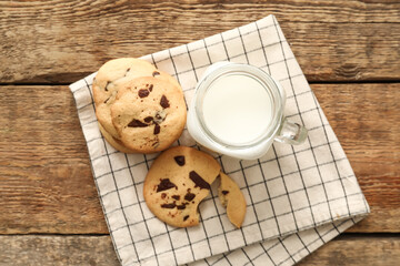 Delicious homemade cookies with chocolate chips and mason jar of milk on wooden background