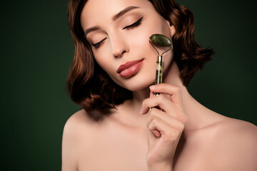 Photo of calm peaceful attractive woman using derma roller on cheek pampering isolated on green color background - obrazy, fototapety, plakaty