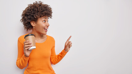 Happy surprised young woman sees something awesome and unexpected indicates at empty blank space...