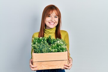 Redhead young woman holding wooden plant pot smiling with a happy and cool smile on face. showing teeth.