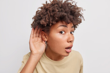 Intrigued curious young woman keeps hand near ear tries to overhear shocking conversation looks...