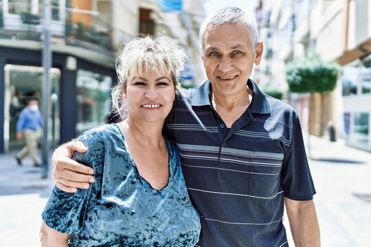 Middle age caucasian couple of husband and wife together on a sunny day outdoors. Smiling happy in love hugging at the city.