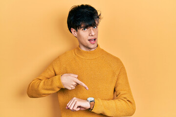 Handsome hipster young man wearing casual yellow sweater in hurry pointing to watch time,...