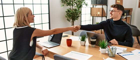 Two business workers smiling happy shaking hands at the office.