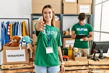 Young blonde girl wearing volunteer t shirt at donation stand smiling friendly offering handshake as greeting and welcoming. successful business.