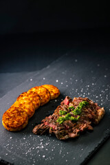 beef steak with potato patties on a dark background