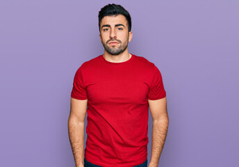 Hispanic man with beard wearing casual red t shirt relaxed with serious expression on face. simple and natural looking at the camera.