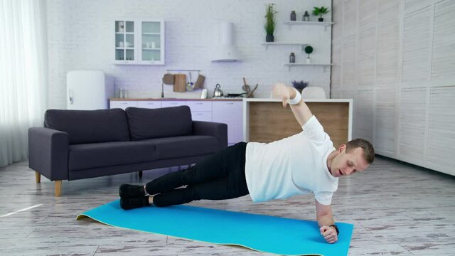 Young man is training at home. Man doing exercise on a mat on kitchen background. Guy working hard to maintain body shape during isolation.