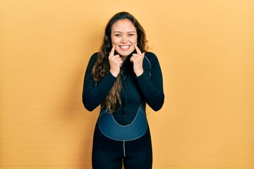 Young hispanic girl wearing diver neoprene uniform smiling with open mouth, fingers pointing and...