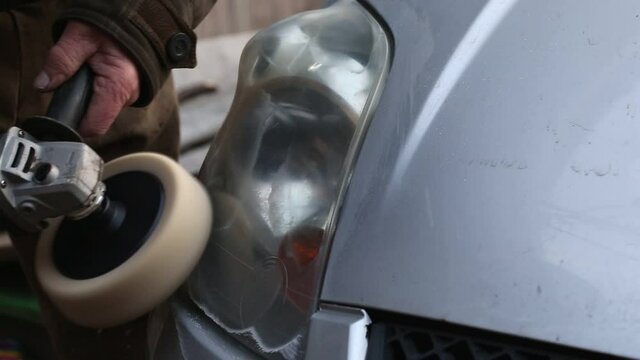 A man polishes a car headlight with a hand grinder.