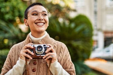 Beautiful hispanic woman with short hair smiling happy outdoors holding vintage camera