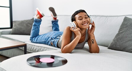 Young hispanic woman listening to music lying on sofa at home