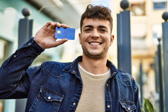 Young hispanic man smiling happy holding credit card at the city