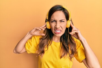 Young latin woman listening to music using headphones clueless and confused expression. doubt...