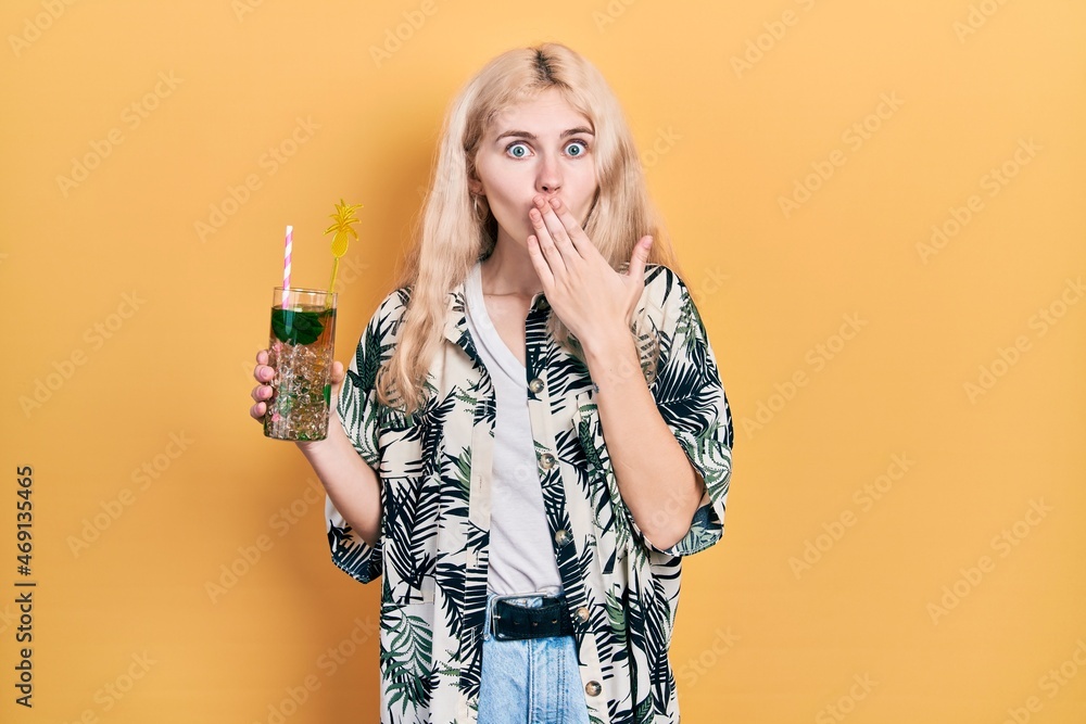 Sticker Beautiful caucasian woman with blond hair drinking mojito glass covering mouth with hand, shocked and afraid for mistake. surprised expression