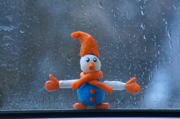 Snowman figurine on the background of a wet window.