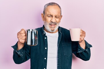 Handsome senior man with beard holding coffee and milk winking looking at the camera with sexy expression, cheerful and happy face.