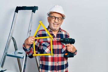 Handsome mature handyman holding screwdriver wearing hardhat by construction stairs winking looking at the camera with sexy expression, cheerful and happy face.