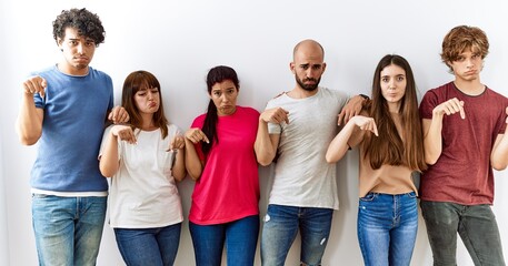 Group of young friends standing together over isolated background pointing down looking sad and upset, indicating direction with fingers, unhappy and depressed.