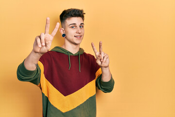 Young caucasian boy with ears dilation wearing casual sweatshirt smiling looking to the camera showing fingers doing victory sign. number two.