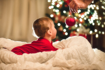 Little baby boy toddler lays and pulls handles to the Christmas ball which holds his tather