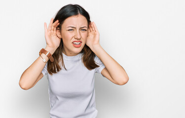 Young beautiful woman wearing casual white t shirt trying to hear both hands on ear gesture, curious for gossip. hearing problem, deaf