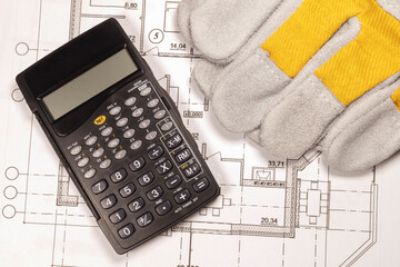 Planning the construction of a house. Construction gloves and calculator on the house plan.