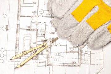 Calculation of the house according to the engineering plan. Work gloves and compasses are on the printed plan of the house.
