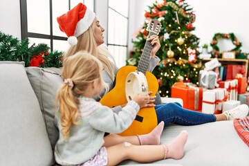 Mother and daughter playing guitar and tambourine sitting by christmas tree at home - obrazy, fototapety, plakaty