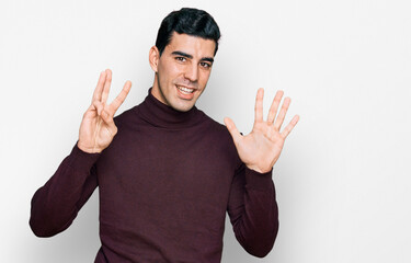 Fototapeta premium Handsome hispanic man wearing casual turtleneck sweater showing and pointing up with fingers number eight while smiling confident and happy.