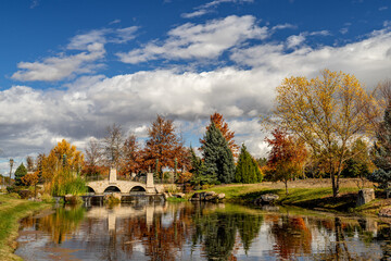 Fototapeta na wymiar Stone bridge leads over a pond with reflection trees