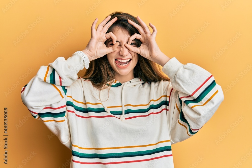 Sticker Young caucasian woman wearing casual clothes doing ok gesture like binoculars sticking tongue out, eyes looking through fingers. crazy expression.