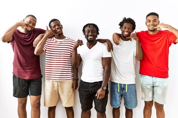 Young african group of friends standing together over isolated background smiling doing phone gesture with hand and fingers like talking on the telephone. communicating concepts.