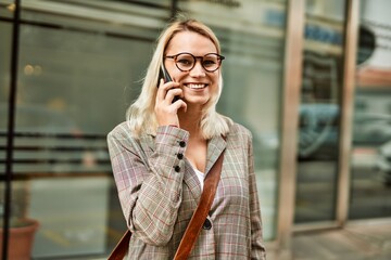 Fototapeta premium Young blonde businesswoman smiling happy talking on the smartphone at the city.