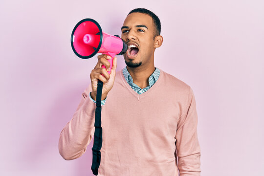 Young african american man shouthing and screaming through megaphone over pink isolated background