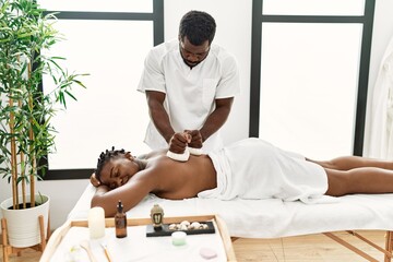 Young african american woman reciving herbal pouches thai massage at beauty center.