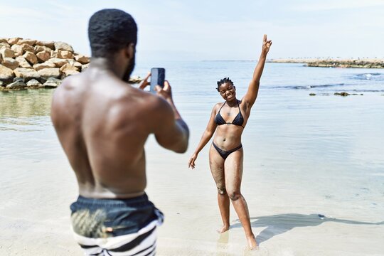 Young african american man making photo to woman using smartphone at the beach.
