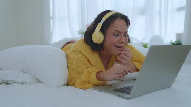 Asian woman woman watching horror movie at home in morning. Single girl in bed wearing headphones watching a scary movie at home. 