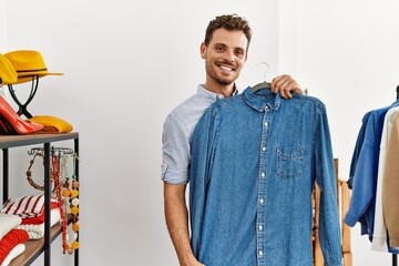 Young hispanic customer man smiling happy holding hanger with shirt at clothing store.