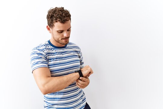 Handsome young man standing over isolated background checking the time on wrist watch, relaxed and confident