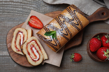 Tasty cake roll with strawberry jam and cream on wooden table, flat lay