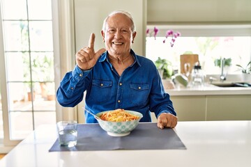 Senior man with grey hair eating pasta spaghetti at home showing and pointing up with fingers number two while smiling confident and happy.