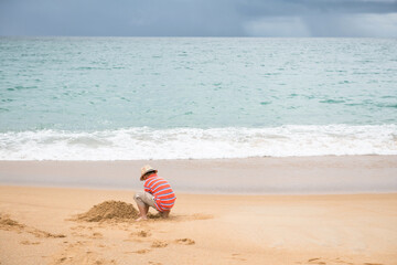 Asian boy with hat make sand castle at beach, Phuket